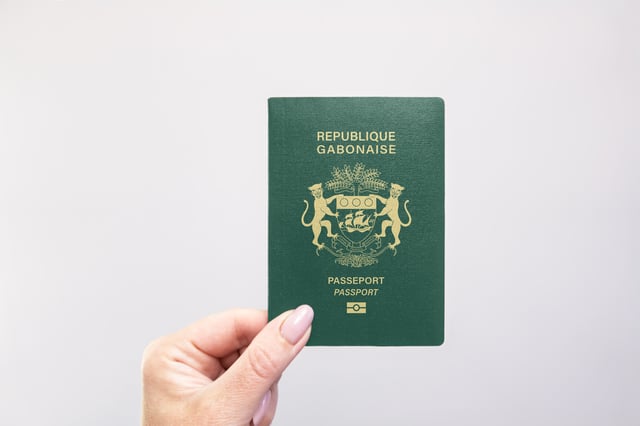 Gabon Passport Held In Hand Against A Plain White Background