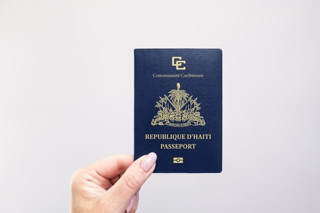 Haiti Passport Held In Hand Against A Plain White Background