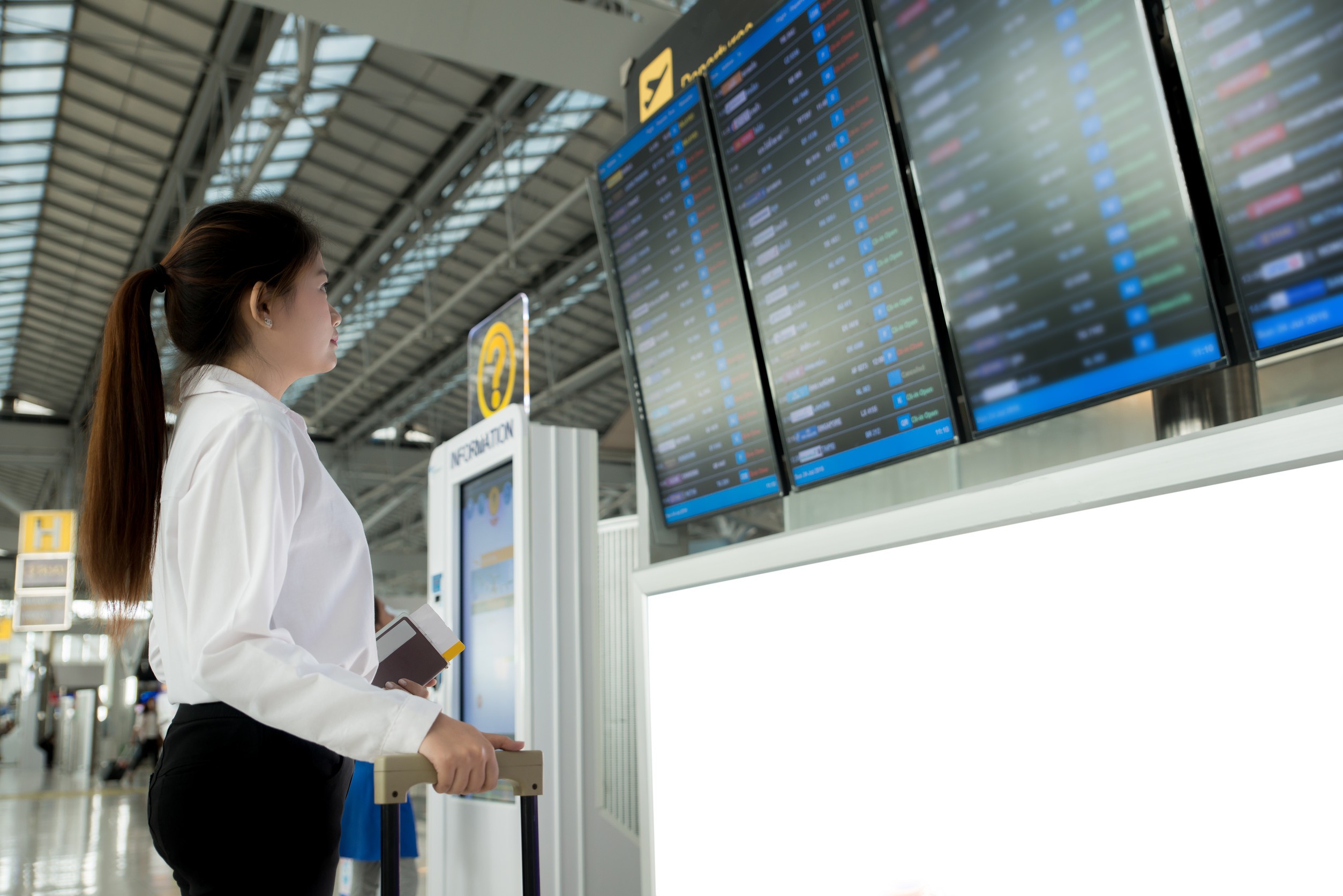 Asian Young Woman In International Airport Looking At The Flight Information Board Checking