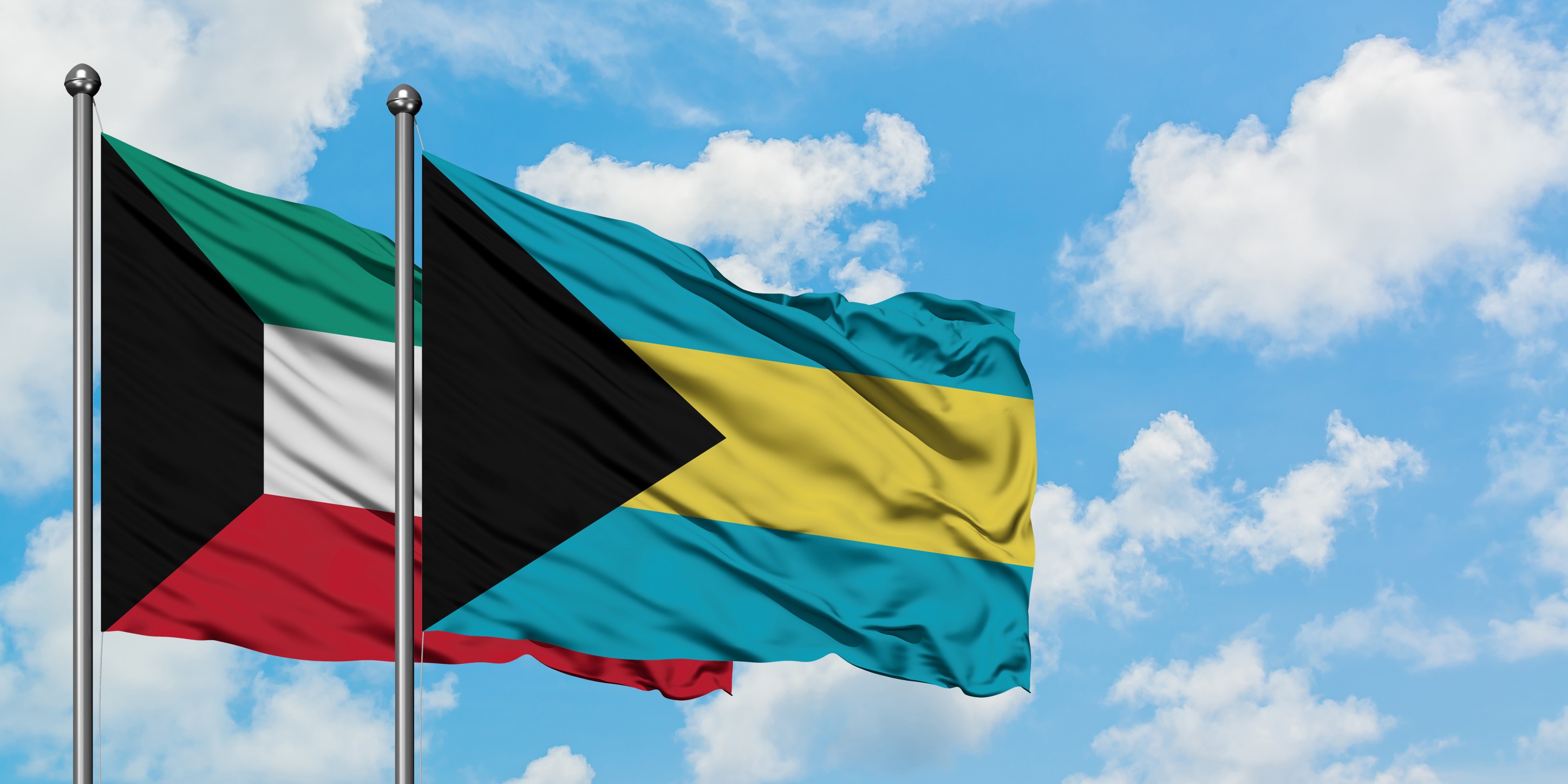 Kuwait And Bahamas Flag Waving In The Wind Against White Cloudy Blue Sky Together